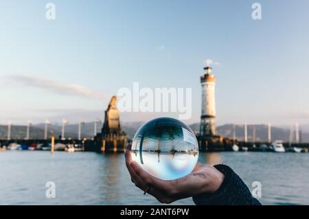 Eine Frau hält eine Glaskugel zwischen dem berühmten Hafeneingang mit Leuchtturm und dem bayerischen Löwen von Lindau, Bodensee Stockfoto