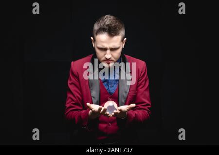 Illusionist Magier zeigt levitation Trick mit Ball in den Händen auf schwarzem Hintergrund Stockfoto