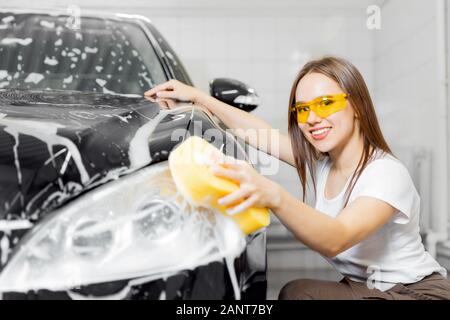 Arbeitnehmer schöne Frau Reinigung Auto black Schaum mit gelben Schwamm. Auto waschen Service Stockfoto