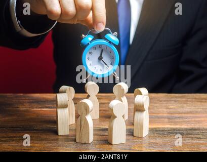 Ein Geschäftsmann hält die Blaue Uhr über ein Team von Mitarbeitern. Zeit-management Konzept. Frist. Teamarbeit. Scrum. Human Resources. Business Meeting. Planni Stockfoto
