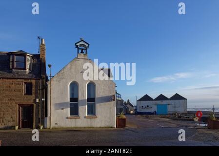 Einer Kreuzung in Johnshaven mit einem alten weißen Kirche mit ihrem Glockenturm und die Fische Kaufmann wirft im Hintergrund. Stockfoto