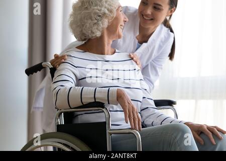 Gerne behinderte ältere Frau sitzt im Rollstuhl, im Gespräch mit Betreuer Stockfoto