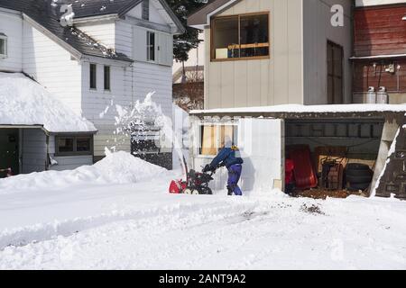Ein japanischer Mann nutzt einen von Hand gepusht Schneepflug oder ein Schneeblower, um an einem Wintermorgen in Yuzawa, Japan, seine Einfahrt zu räumen. Stockfoto