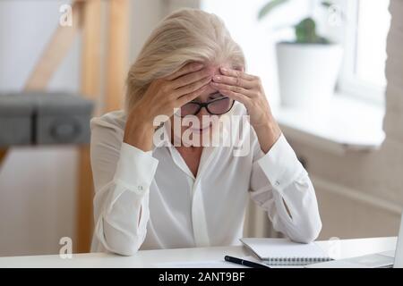 Im Alter von ungesunden Geschäftsfrau touch Stirn leidet unter Migräne Stockfoto