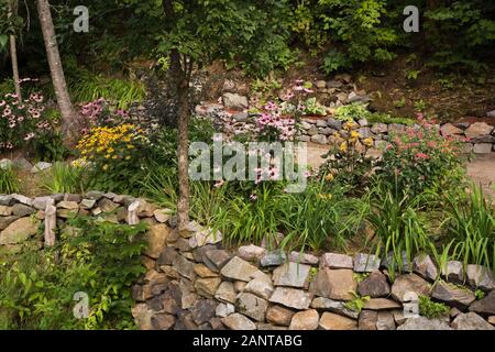 Erhöhte Steingrenze mit gelben Rudbeckias und lila Echinacea purpurea - Kegelblumen in privaten Vorgarten im Sommer Stockfoto