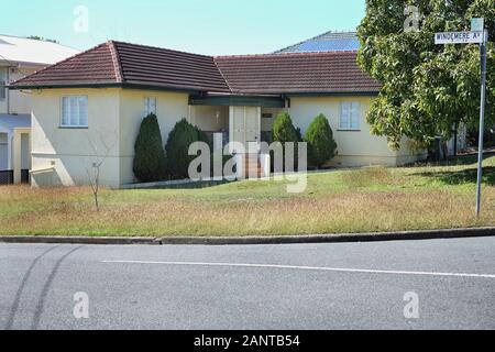 Ein originales, L-förmiges Nachkriegsgebäude in einem grasbewachsenen Eckblock mit kleinen Nadelbäumen, die die Eingangstür flankieren, im Vorort Cannon Hill in Brisbane Stockfoto