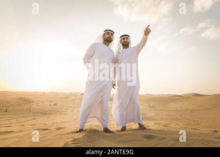 Arabische Männer witk kandora Wandern in der Wüste - Porträt von zwei mittleren Osten Erwachsene mit traditionellen arabischen Kleid Stockfoto