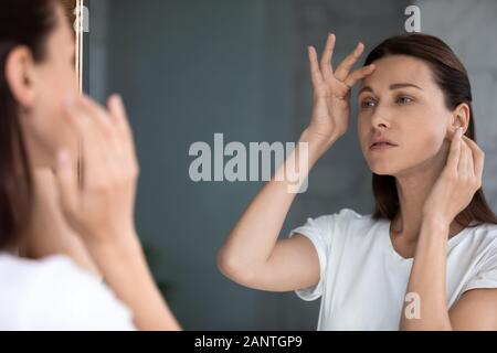 In dem Bestreben, Frau im Spiegel zu betrachten, berühren die Stirn, über Falten verwirrt Stockfoto