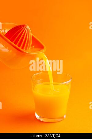 Entsafter gießen Orangensaft in ein Glas, orange Hintergrund mit Platz für Kopie Stockfoto