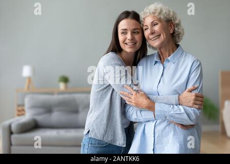 Gerne Großmutter und Enkelin umarmen, im Wohnzimmer stehend Stockfoto