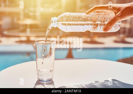 Frau Hand gießt Wasser in Glas aus Kunststoff Flasche gegen Schwimmbad Hintergrund Stockfoto