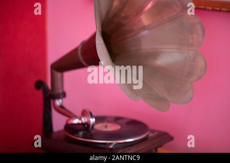 Ein alter Grammophon- oder Phonographen-Plattenspieler, der gegen eine rosafarbene Wand fotografiert wurde, mit selektivem Fokus auf den bläserförmigen Lautsprecher Stockfoto