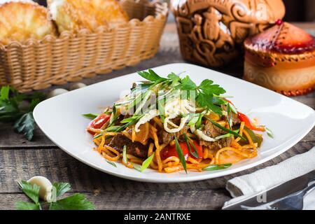 Traditionelle asiatische usbekischen Nudel lagman mit Gemüse und Fleisch auf rustikalen Holztisch Hintergrund. Close-up Stockfoto