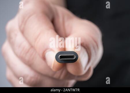 USB Typ C Stecker mit einem grauen Kabel in der Hand gehalten wird. Geringe Tiefenschärfe. Stockfoto