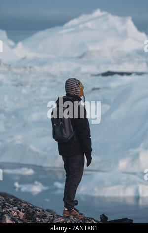 Grönland touristische Mann Explorer mit Blick auf den Eisfjord in Ilulissat. Reisen in die arktischen Landschaft Natur mit Eisbergen. Touristische Person suchen und mit unglaublicher v Stockfoto