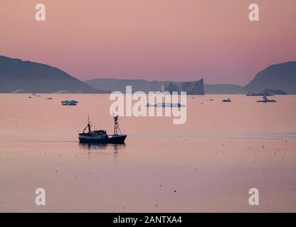 Fisch Trawler zwischen riesigen eisbergen während der mitternachtssonne mit Sonnenuntergang und Sonnenaufgang am Horizont. Fischerboot im Arktischen Ozean Wasser. Foto im Greenla genommen Stockfoto