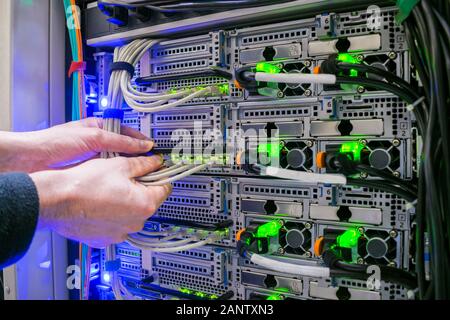 Wartungsarbeiten im Rechenzentrum Serverraum. Die Hand eines Techniker mit einem Kommunikation Internet Kabel ist ein Close-up. Anschluss der stammkabel zu Stockfoto