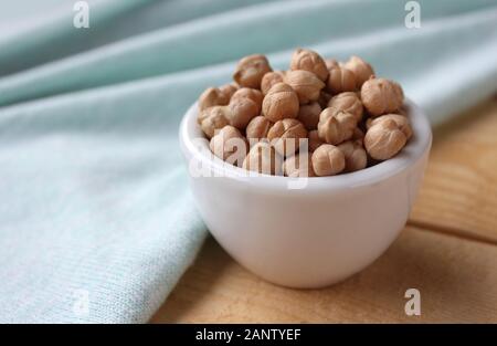 Seite Blick auf einer weißen Schüssel gefüllt mit Kichererbsen (Cicer arietinum), auf einem Holztisch mit mint grün Tischdecke. Mit Copyspace. Stockfoto