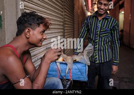 Zwei fröhliche, scherzende junge Migranten aus Uttar Pradesh (Nordindien) auf dem Crawford-Markt, Mumbai, Indien, einer hat seinen frühen Morgentee Stockfoto