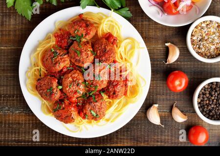 Gebratene Fleischbällchen und Spaghetti auf dem Teller, Tomatensauce und Gewürz auf Holztisch. Ansicht von oben, flach Stockfoto