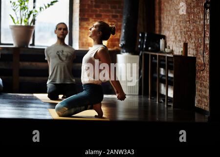 Yoga-Klasse junge, übergewichtige Frau, die praktizierende Posen trainiert, die den Körper ausdehnen und im Fitnessstudio einen gesunden Lebensstil mit Gewichtsverlust genießen Stockfoto