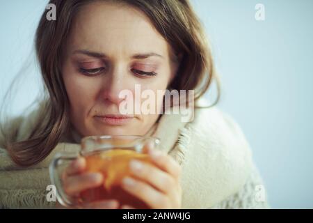 Portrait von Sad sick modernen mittleren Alter Frau in Rollkragen Pullover und Strickjacke trinken heiße Tasse Tee mit Ingwer, Zitrone und Honig isoliert auf Winter Stockfoto