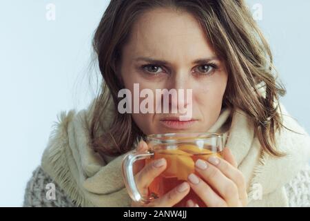 Portrait von unglücklichen Kranken elegante 40 Jahre alte Frau in Rollkragen Pullover und Strickjacke trinken heiße Tasse Tee mit Ingwer, Zitrone und Honig isoliert auf Stockfoto