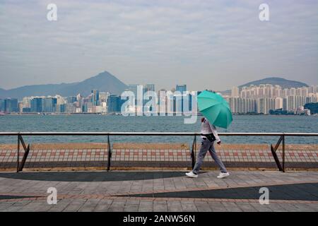 Eine Frau mit einem Regenschirm läuft die Quarry Bay Promenade am Ufer des Victoria Harbour in Hongkong. Stockfoto