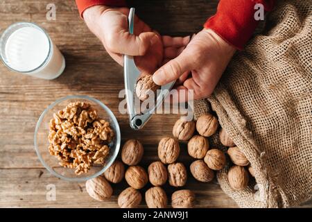 Ganze Walnüsse in einer Baumwolltasche, verstreute Muttern auf einer hölzernen Tisch. Walnusskerne in eine Schüssel geben. Stockfoto