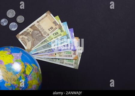 Kopf auf Schuss von indischen Banknoten von 10.20.50.100.500 Rupien und Münze oder Pfennig mit einem Weltkarten-Globus auf schwarzem Hintergrund mit Kopierraum für Text. Stockfoto