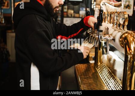 Barkeeper Bier in einer Bar. Bärtige mutiger Mann gießt sie einem Schäumenden Getränk. Stockfoto