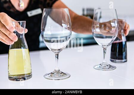 Weibliche Barkeeper Hände auf kleine mini Dekanter mit roten und weißen Weinen gefüllt. Neben zwei Wein leere Gläser auf hellen, weißen Tasting Room Bar Counter Stockfoto