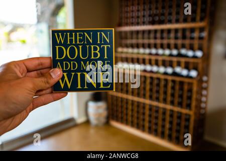 Wenn im Zweifel mehr Wein hinzufügen, Hand zitat Zeichen selektiven Fokus Ansicht gegen Wein Tasting Room interior Weine shop Flaschen in den Regalen Hintergrund Stockfoto