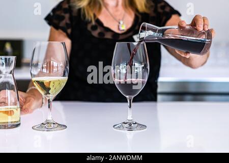 Weibliche Barkeeper hand Nahaufnahme, wie Sie gießen Rotwein aus einer kleinen Mini decanter zum WINEGLASS, neben einem weißen Glas Wein, helle Bar Counter Stockfoto