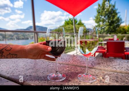 Tätowierte hand Rotwein Glas, rote und weiße Weine Gläser schließen bis auf eine Tabelle der Weingut Keller Probierstube Terrasse, Okanagan Lake Hintergrund Stockfoto