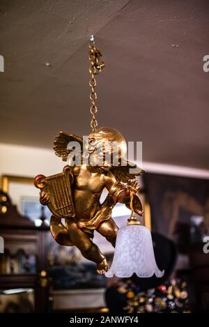 Statue des Engels. Goldener Engel. Eine Blumenarrangement, die von der Decke hängt und mit Holzhintergrund aus der Lampe aufleuchtet. An der Kette alte Vintage House Artikel Verkauf Garage Stockfoto