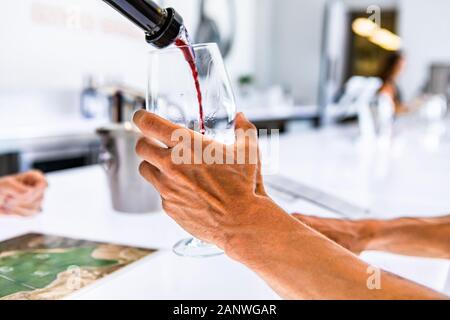 Roter wein Ausgießen aus der Flasche an den Kunden wineglass selektiven Fokus, Nahaufnahme, isoliert, frische Farben mit Bar weiße LED-Leuchten Hintergrund Stockfoto