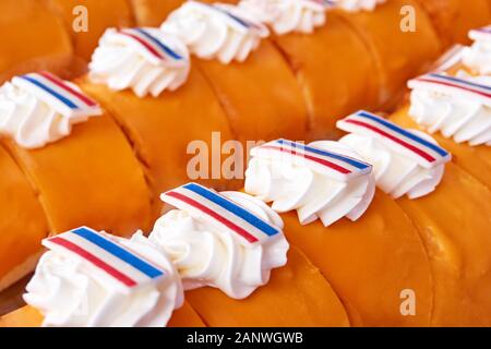 Gebäckreihen mit orangefarbener Glasur, Schlagsahne und essbaren Etiketten mit holländischen Flaggen auf Koningsdag in den Niederlanden. Stockfoto