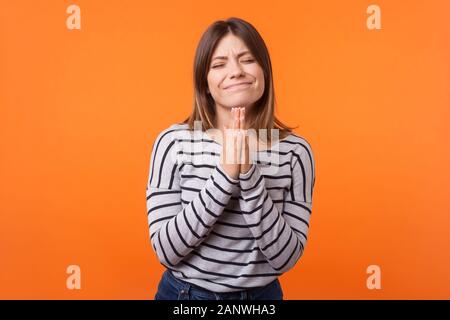 Bitte, lassen Sie es geschehen! Porträt der hoffnungsvolle junge Frau mit braunen Haaren in Long Sleeve Striped Shirt stehend, Hände halten im Gebet und machen möchten. ind Stockfoto