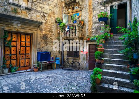 Schöne schmale Straße mit Häusern aus Stein. Alte Steinhäuser und Eingänge mit Blumen geschmückt. Gemütliche Apartments und gepflasterte Strasse mit blumigen Entran Stockfoto
