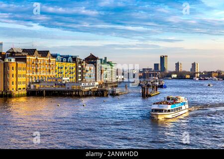 Am Ufer der Themse, von der Tower Bridge aus gesehen, mit Blick nach Osten in Richtung St Katherine's and Wapping, London Eye River Cruise Boat voller Touristen, London, Großbritannien Stockfoto