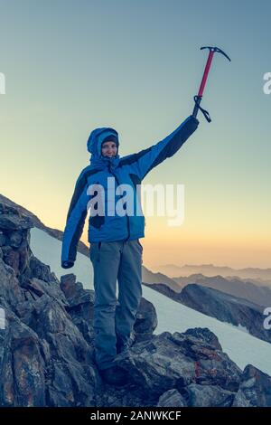 Weibliche Bergsteiger feiert erfolgreiche Aufsteigen mit Eispickel angehoben in den Himmel. Stockfoto