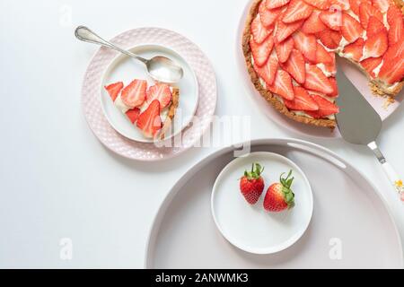 Eine köstliche, frische Kuchen mit Pudding Sahne und Erdbeeren. Ein Stück gerieben auf einem rosa Platte. Alles auf einem weißen Tisch. Stockfoto