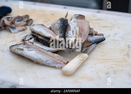 Kleiner Fisch neben dem weißen Messer auf weißem Schneidebrett Stockfoto