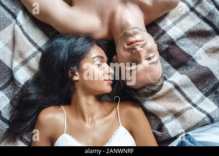 Mixed Race Paar. Junge Mann und die Frau zu Hause auf dem Bett liegend auf der Suche Kamera glücklich oben viewe clsoe-up Stockfoto