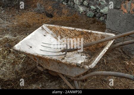 Dirty Schubkarre auf Landschaft, vielleicht auf einem Bauernhof, die im Inneren mit Rechen Stockfoto