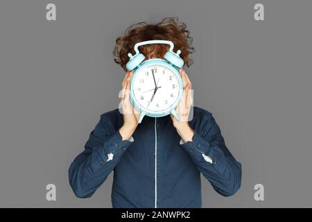 Zeit angezeigt. Teenager Junge auf Grau für Gesicht mit Wecker isoliert Stockfoto