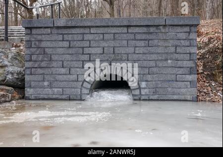 Wasserdurchlass im Freien durch eine Mauer gefroren und durch Eis blockiert Stockfoto