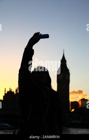 Silhouette von Mädchen unter selfie mit Big Ben im Hintergrund bei Sonnenuntergang, South Bank, London, England. Fokus auf Mädchen. Stockfoto