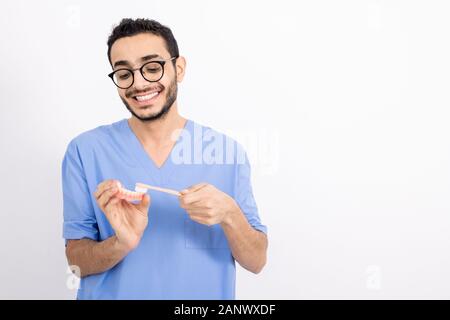 Junge Zahnarzt in Uniform falsche Zähne putzen mit der Zahnbürste in der Isolation Stockfoto